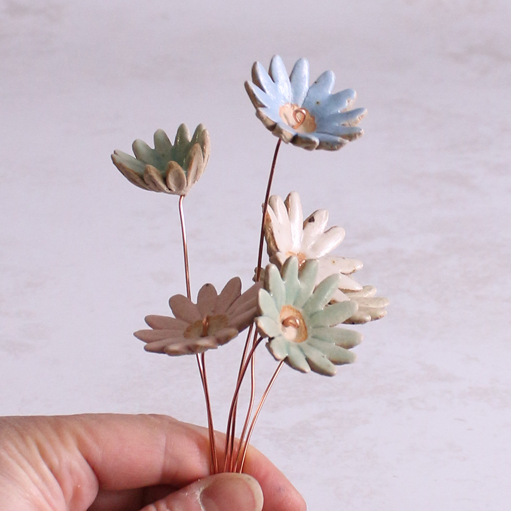 Several handmade ceramic daisy flower stems in various pastel glazes, creating a colourful ceramic bouquet.