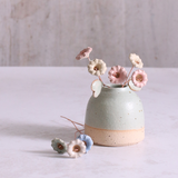 A bouquet of ceramic wildflower stems in pastel shades of pink, blue, and white, artfully arranged in a rustic ceramic vase and some laid next to the vase.