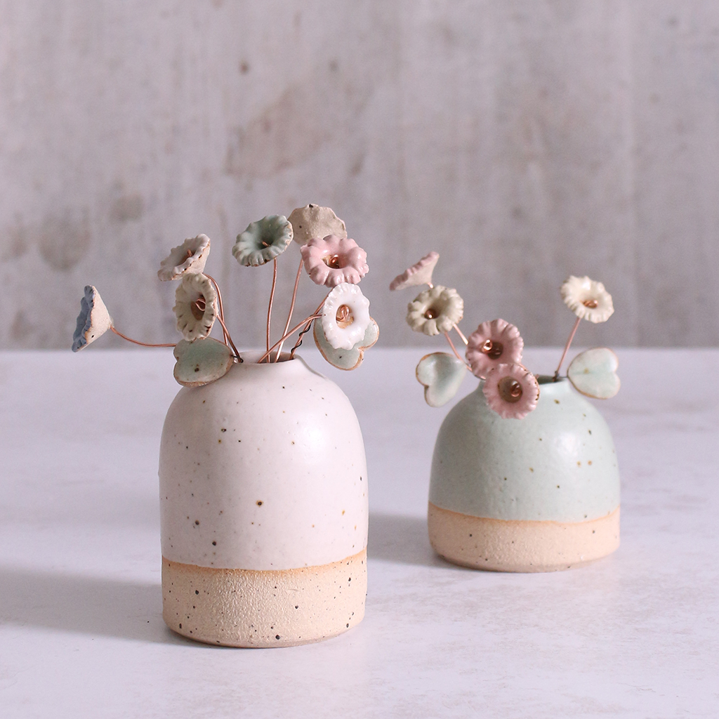 A bouquet of ceramic wildflower stems in pastel shades of pink, blue, and white, artfully arranged in two rustic ceramic vases, highlighting the versatility of these handmade floral decorations.