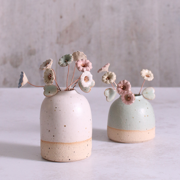 A bouquet of ceramic wildflower stems in pastel shades of pink, blue, and white, artfully arranged in two rustic ceramic vases, highlighting the versatility of these handmade floral decorations.