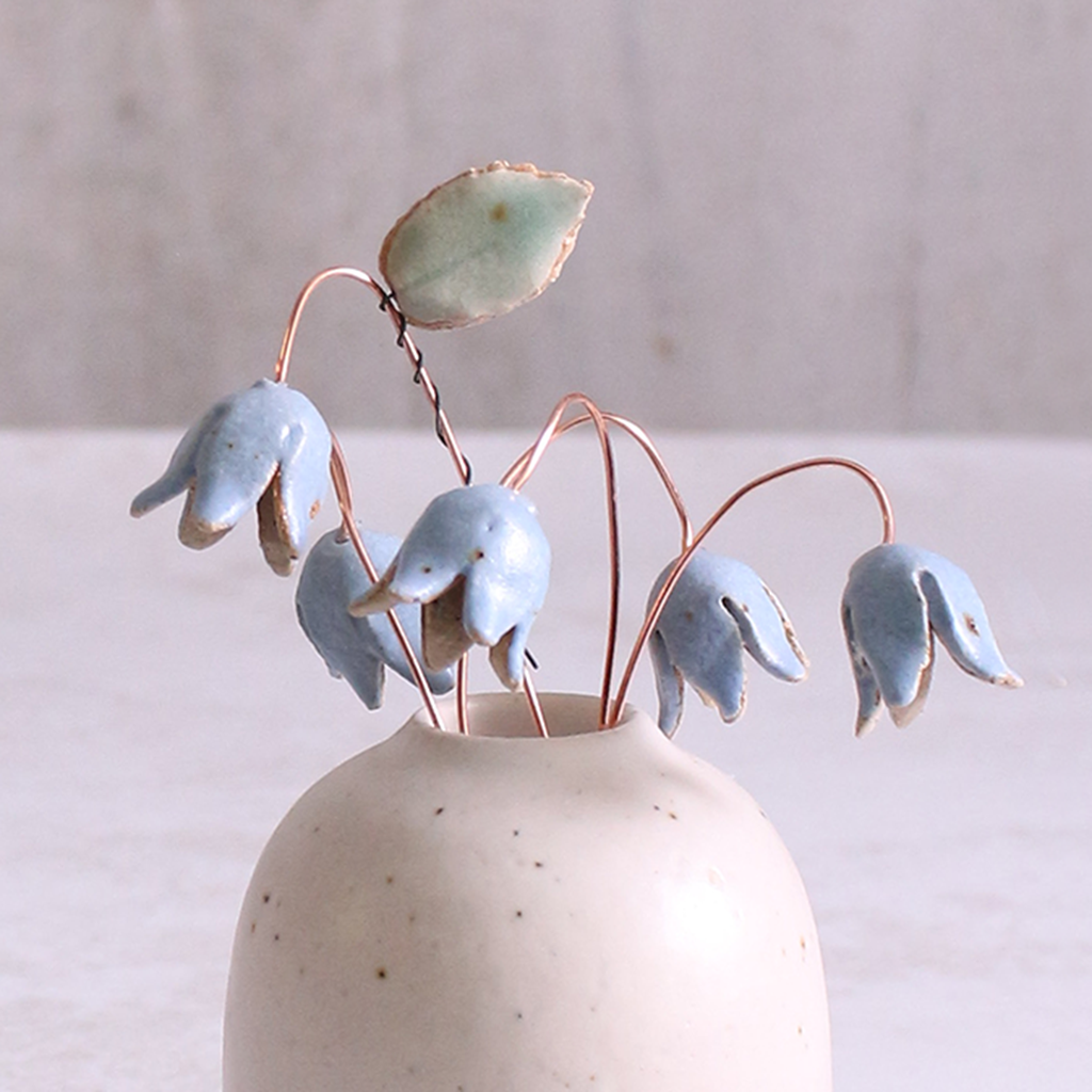 Handcrafted ceramic bluebell flower stems with soft glazes displayed in an off-white vase. Each flower features a flexible copper wire stem for easy adjustment.