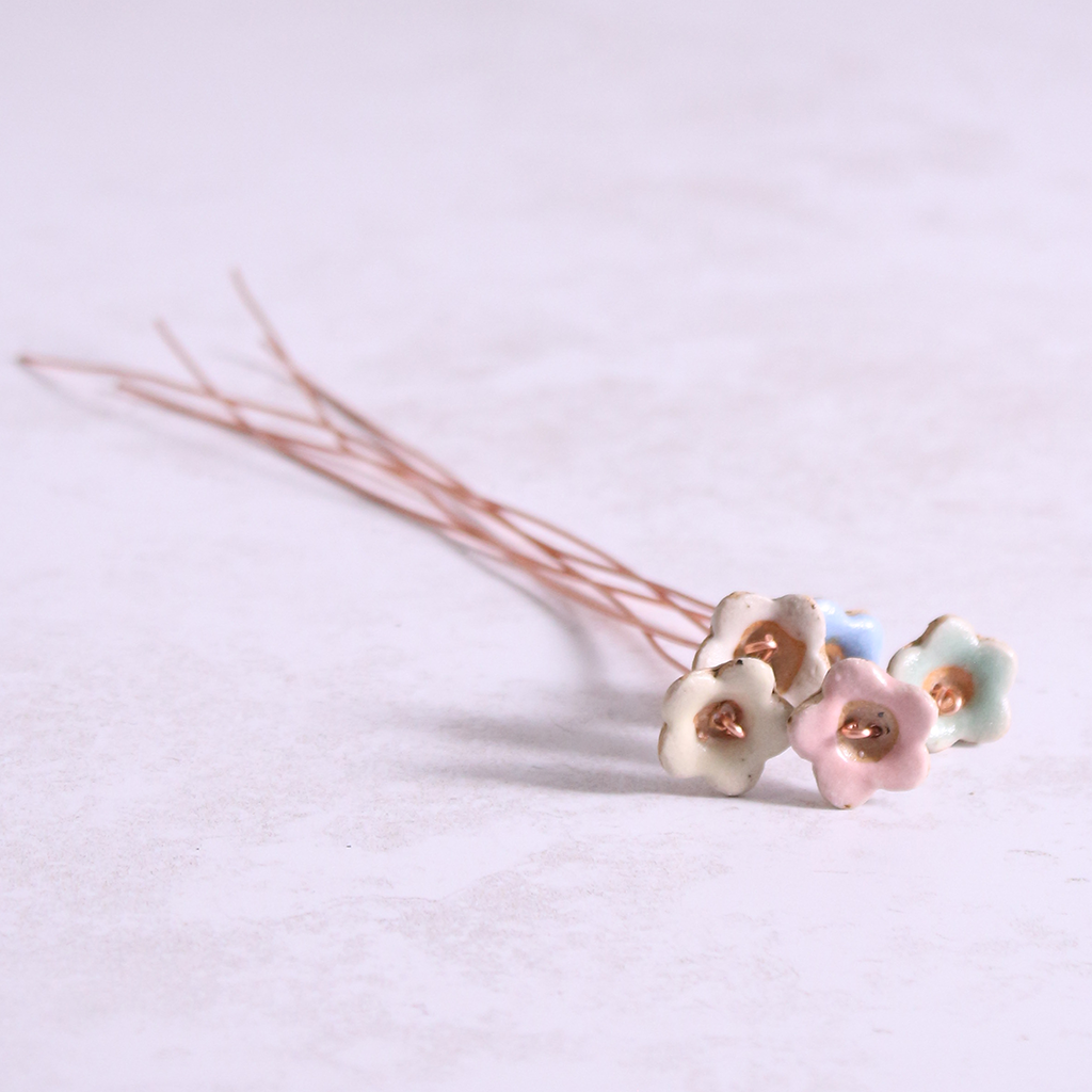Close-up of table with pastel ceramic flower stems with copper wire stems lay on it – individually handcrafted floral home accessories from Habulous