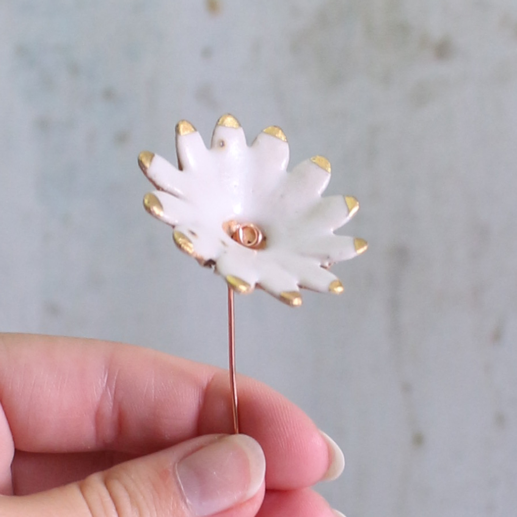 White ceramic flower with gold accents held by a hand against a neutral background