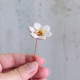 White flower-shaped brooch held by a hand against a neutral background