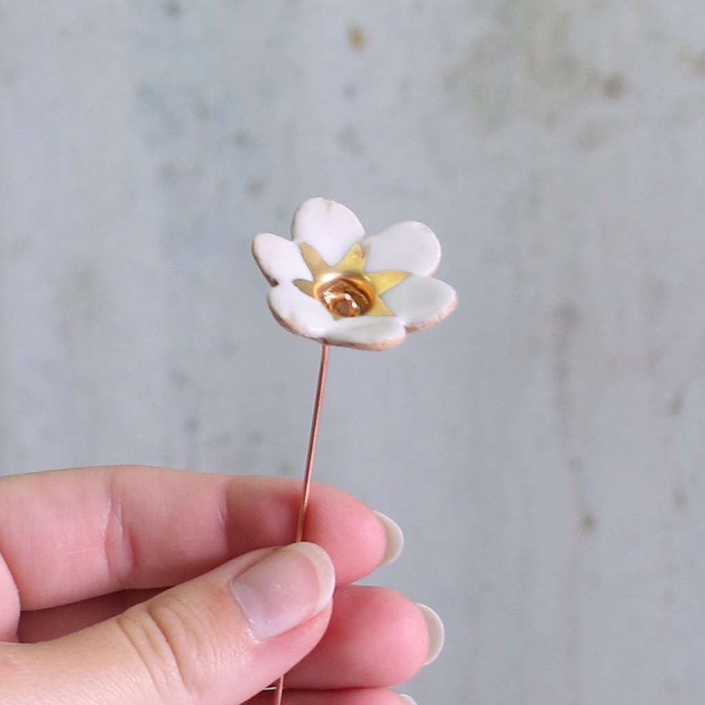 White flower-shaped brooch held by a hand against a neutral background