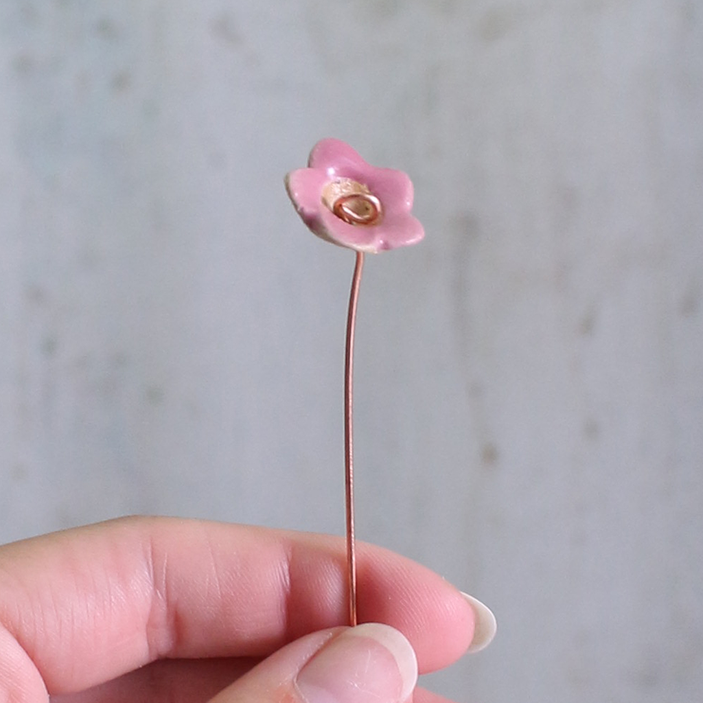 Pink flower  on a thin flexible wire held by a hand against a grey background