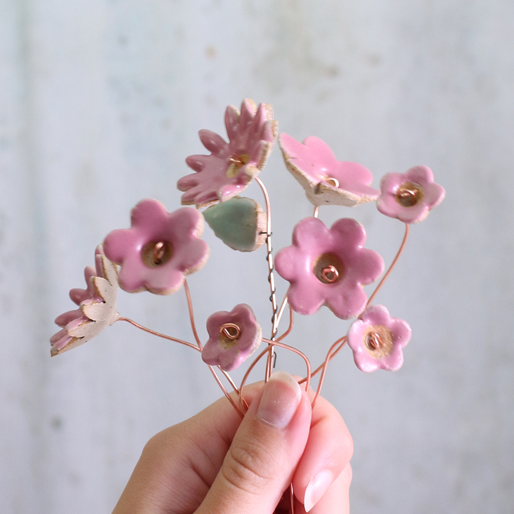 Hand holding a ceramic bouquet with pink flowers against a light background