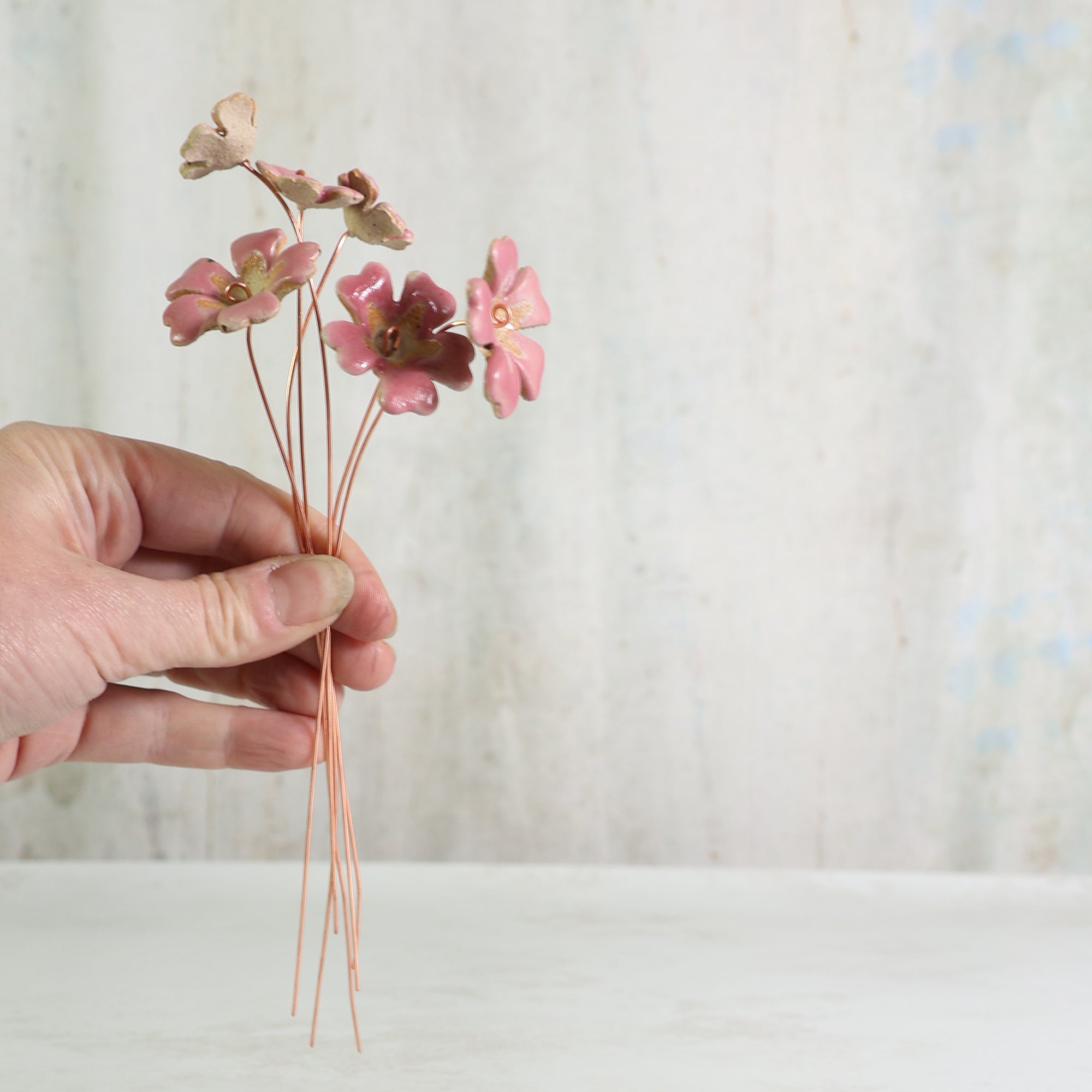 Hand holding a small bouquet of eramic pink primrose flowers against a neutral background