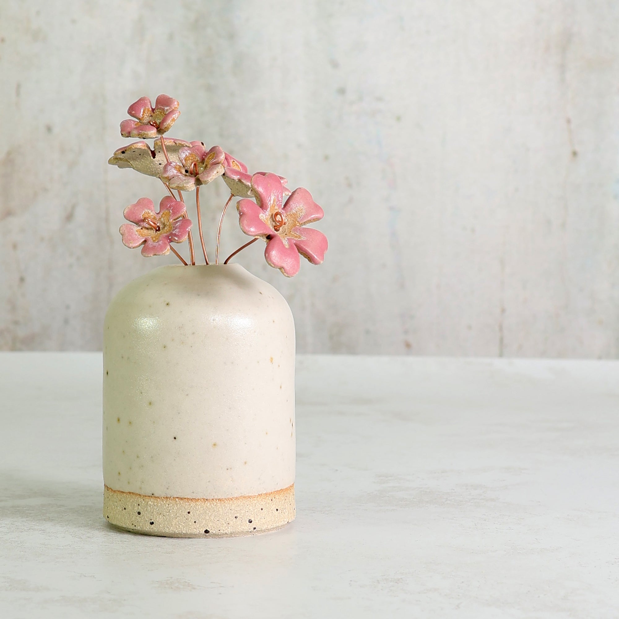 White ceramic vase with speckled texture holding pink ceramic flowers on a light background