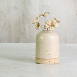 Small ceramic vase with speckled texture holding ceramic primrose flowers on a light background