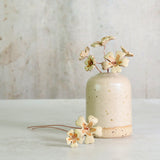 Beige ceramic vase with ceramic flowers on a light wooden surface