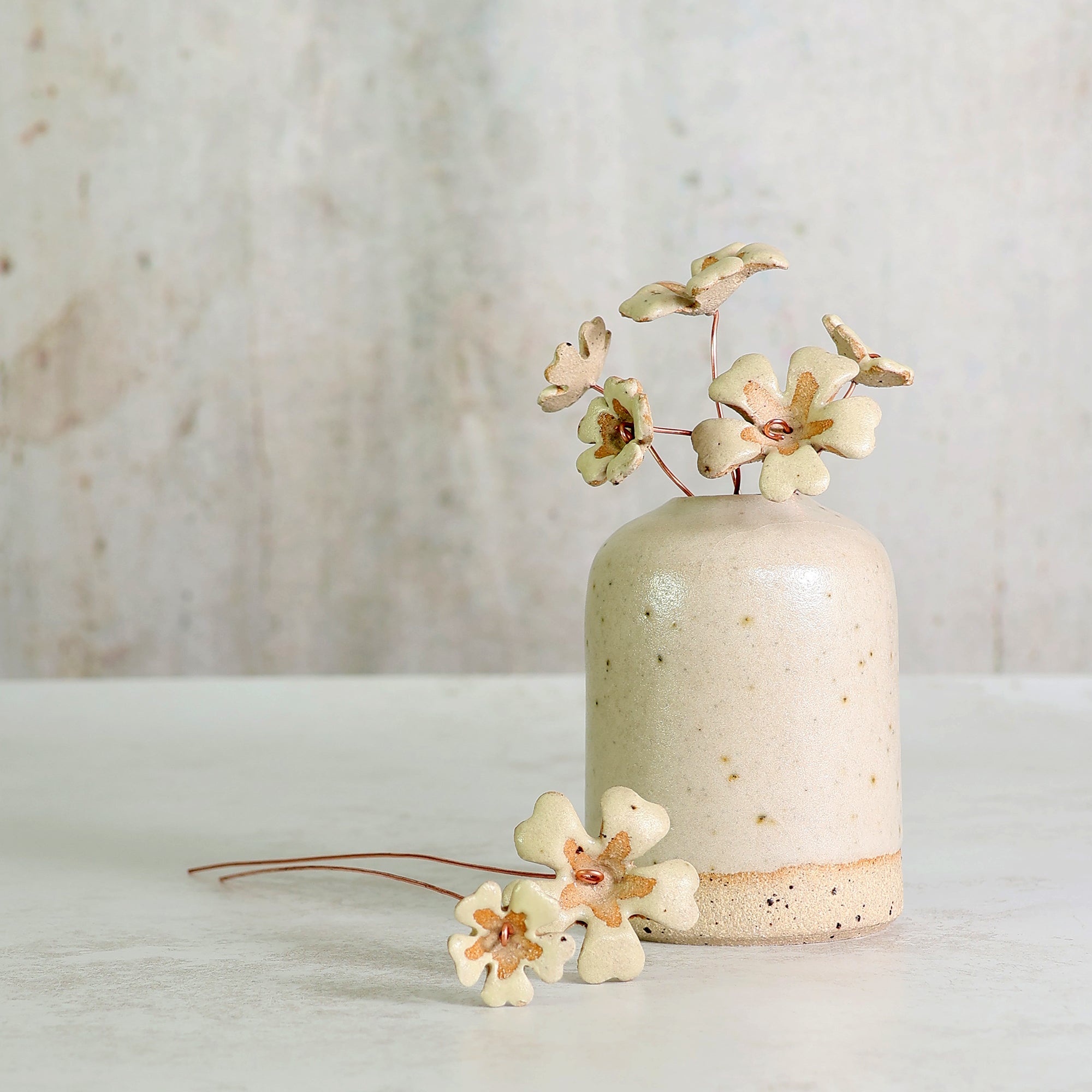 Beige ceramic vase with ceramic flowers on a light wooden surface