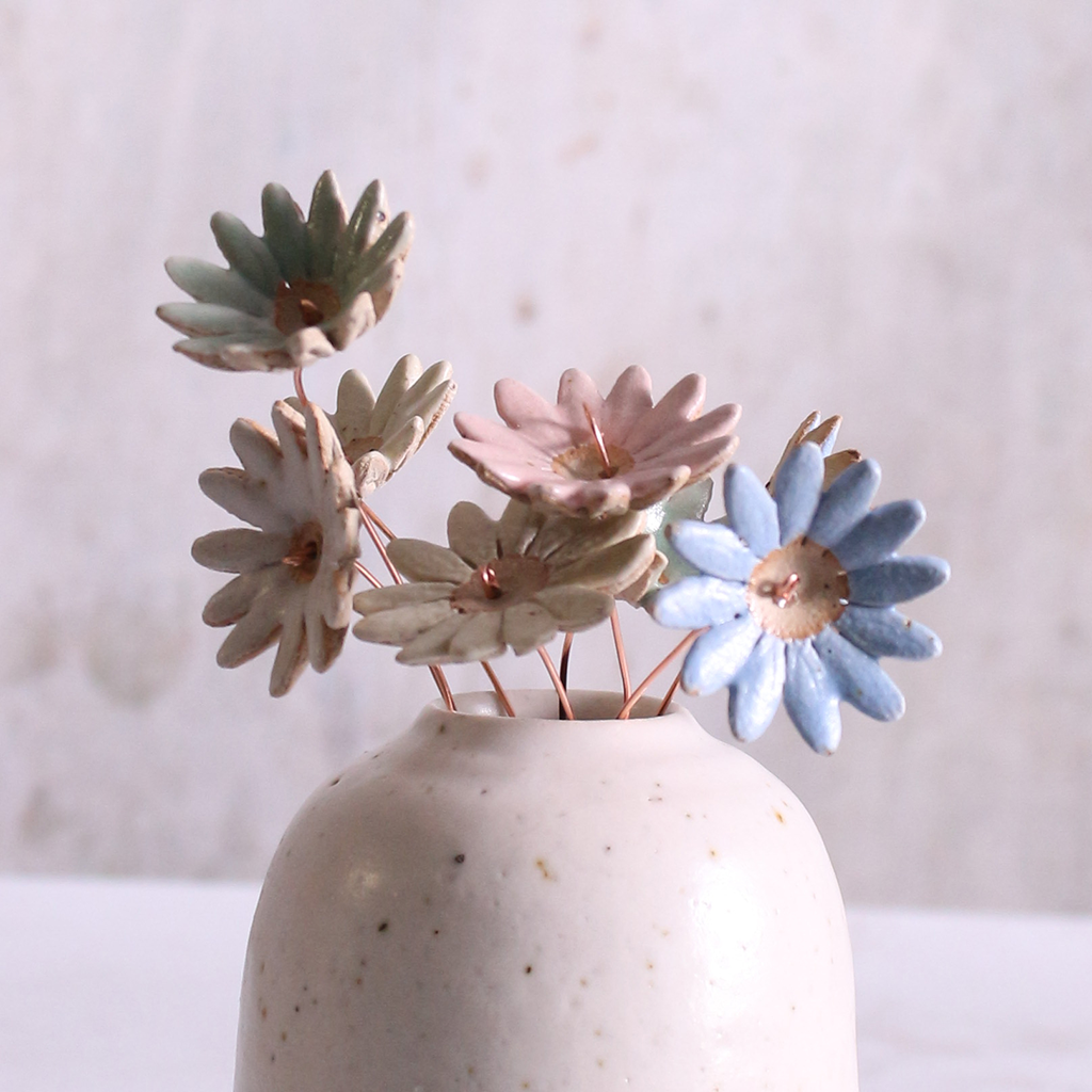 Handmade soft pastel glaze ceramic daisy flower stems displayed in an off-white vase.