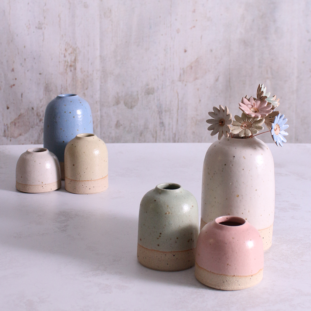A bouqet of handmade ceramic daisy flower stems in vases with different pastel glazes, creating a colourful display.