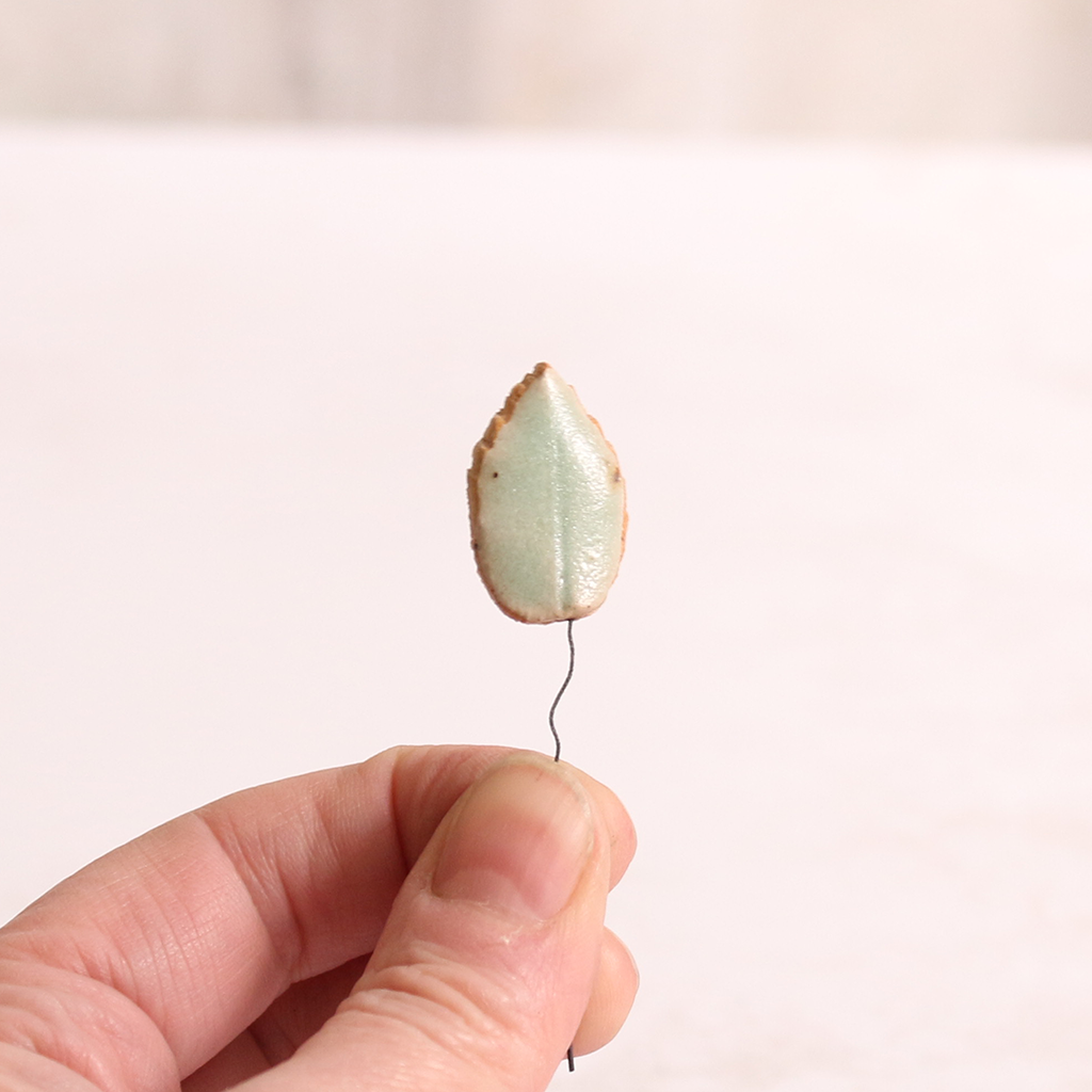 Close up of small ceramic leaf being held in someone's hands.
