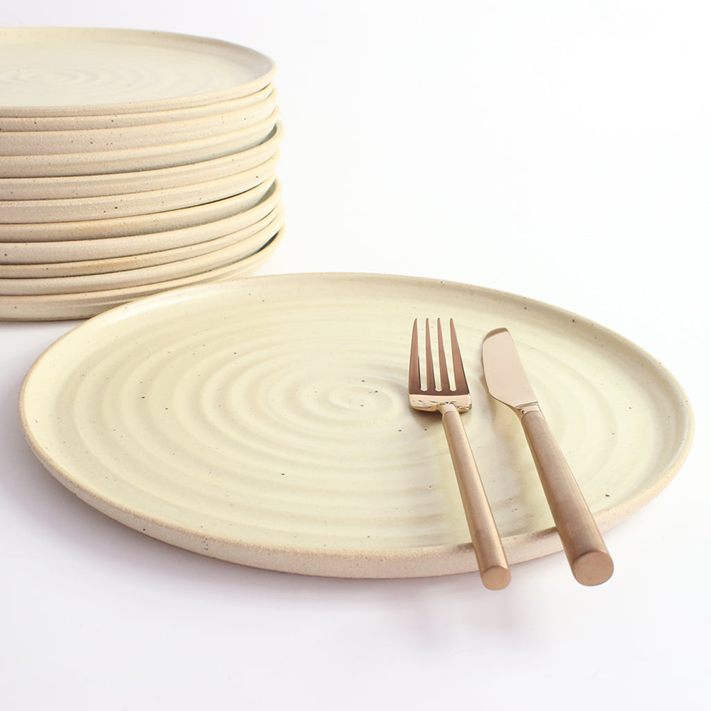 Yellow dinner plate with copper cutlery next to stack of plates