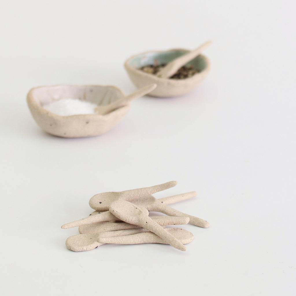 Pile of mini clay spoons in front of salt and pepper bowls with spoons