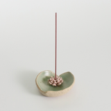 Ceramic incense holder with a single incense stick on a light gray background