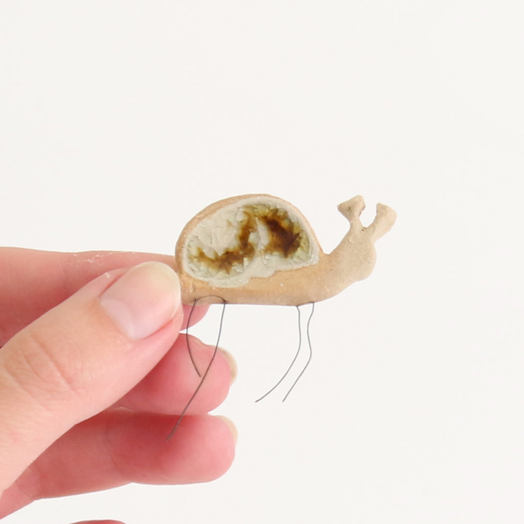 hand holding small ceramic and glass snail plant hugger