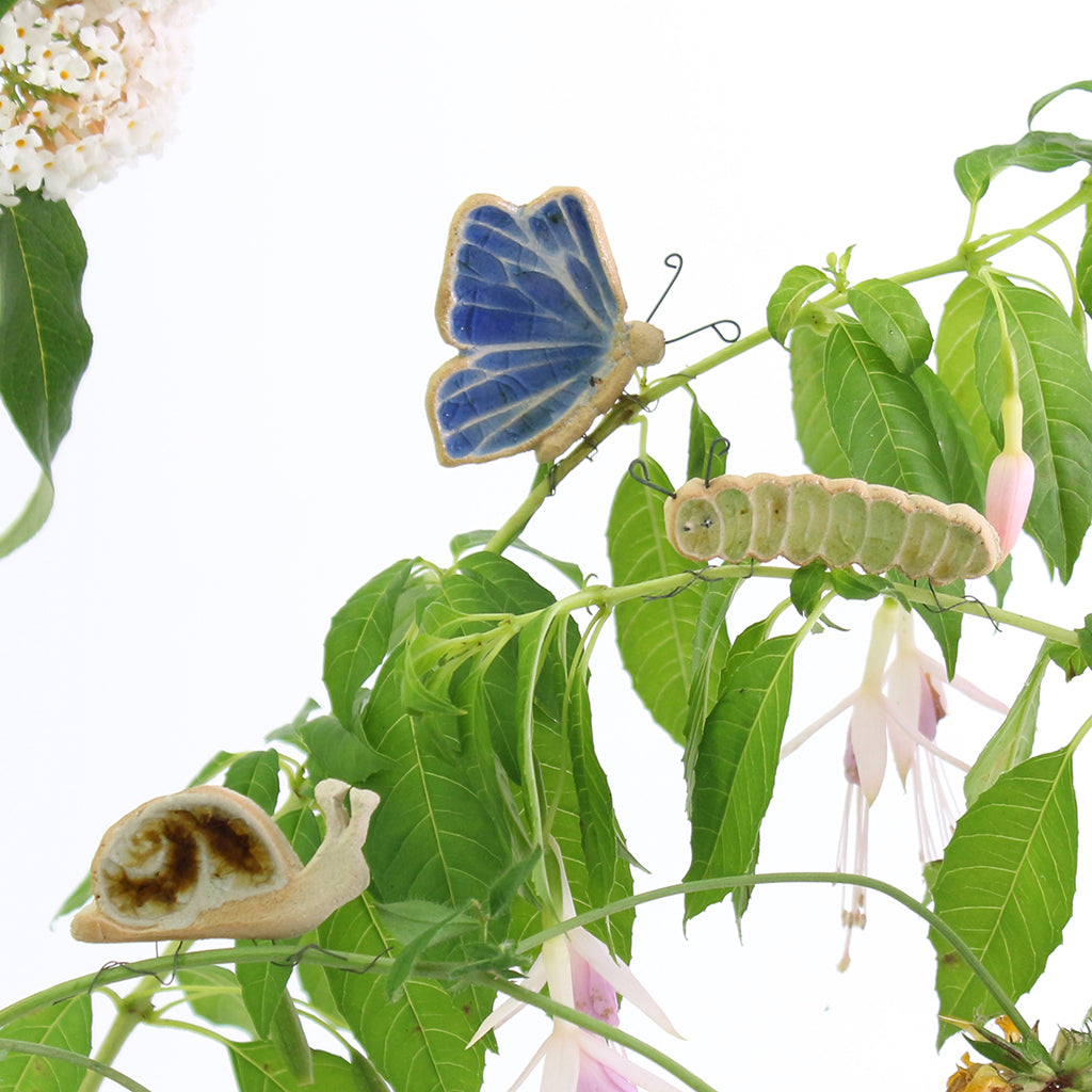 small ceramic and glass blue butterfly, green caterpillar and brown snail plant decorations on plant stems