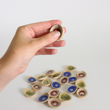 Hand holding a small ceramic worry stone with a collection of similar items on a light surface