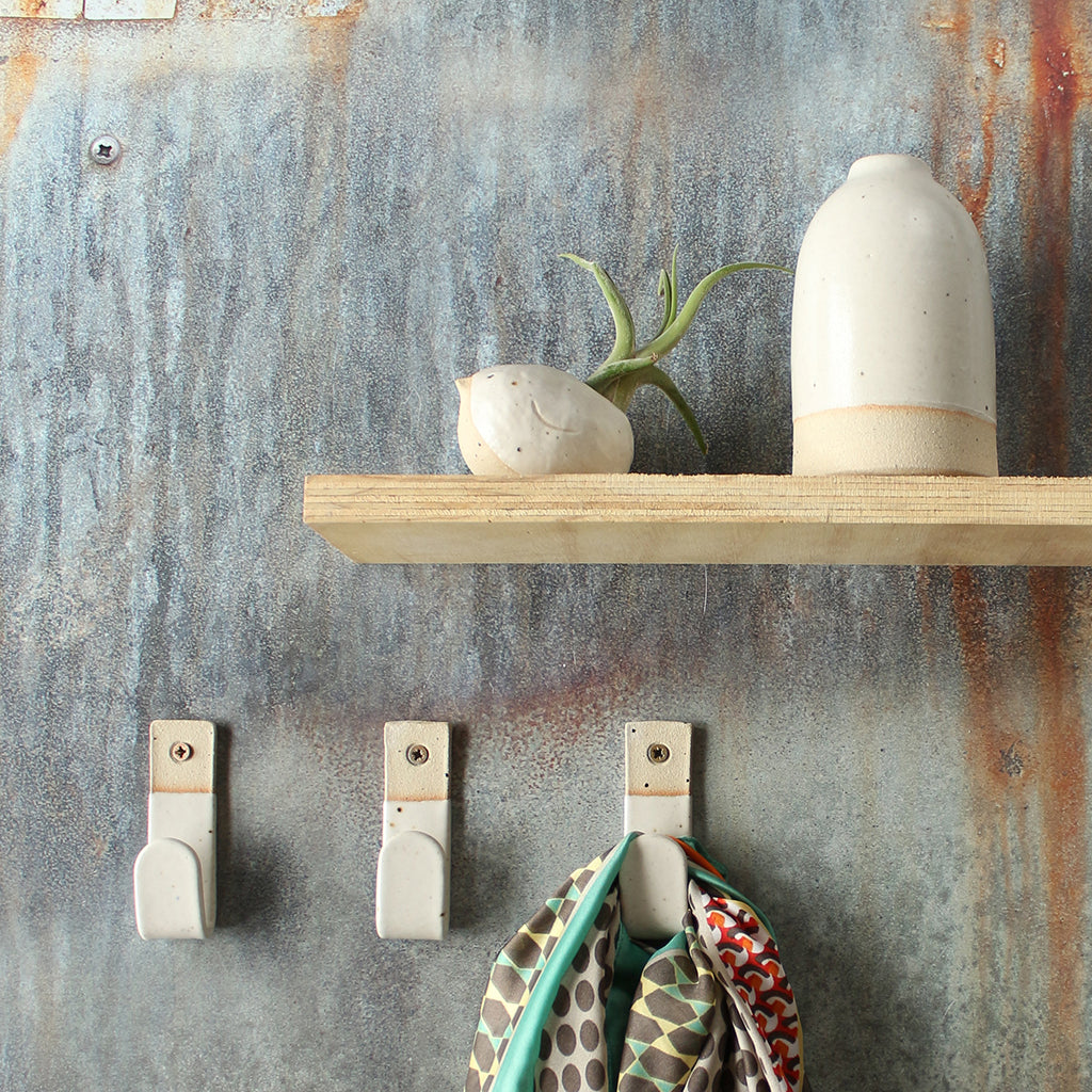 3 white wall hooks, one holding a scarf, with white decor