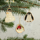 Three Christmas ornaments shaped like a snowman, a robin, and a penguin hanging from a tree.