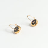 Gold hoop earrings with black circular charms on a white background