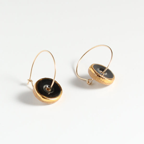 Gold hoop earrings with black circular charms on a white background