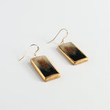 Rectangular earrings with gold lustre and eclipse colours on a light gray background