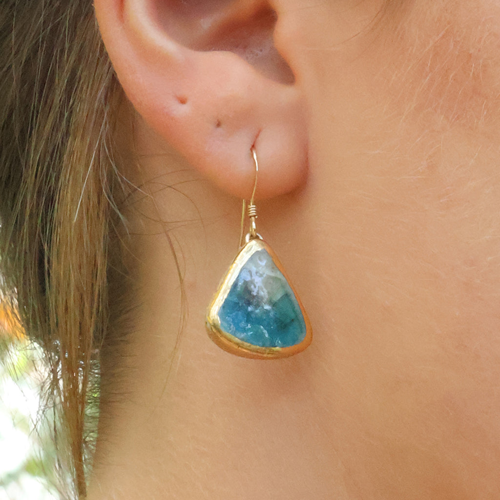 A women wearing a teardrop earring made from ceramic and teal glass with gold detailing. 