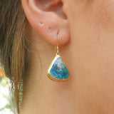 A women wearing a teardrop earring made from ceramic and teal glass with gold detailing. 