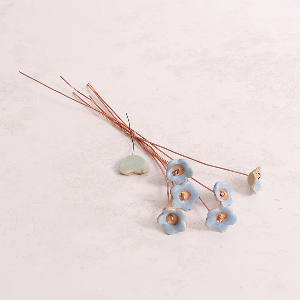 Close-up of pastel ceramic forget me not flower stems with copper wire stems on a table  – individually handcrafted floral home accessories from Habulous