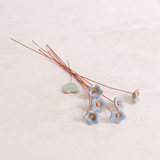Close-up of pastel ceramic forget me not flower stems with copper wire stems on a table  – individually handcrafted floral home accessories from Habulous
