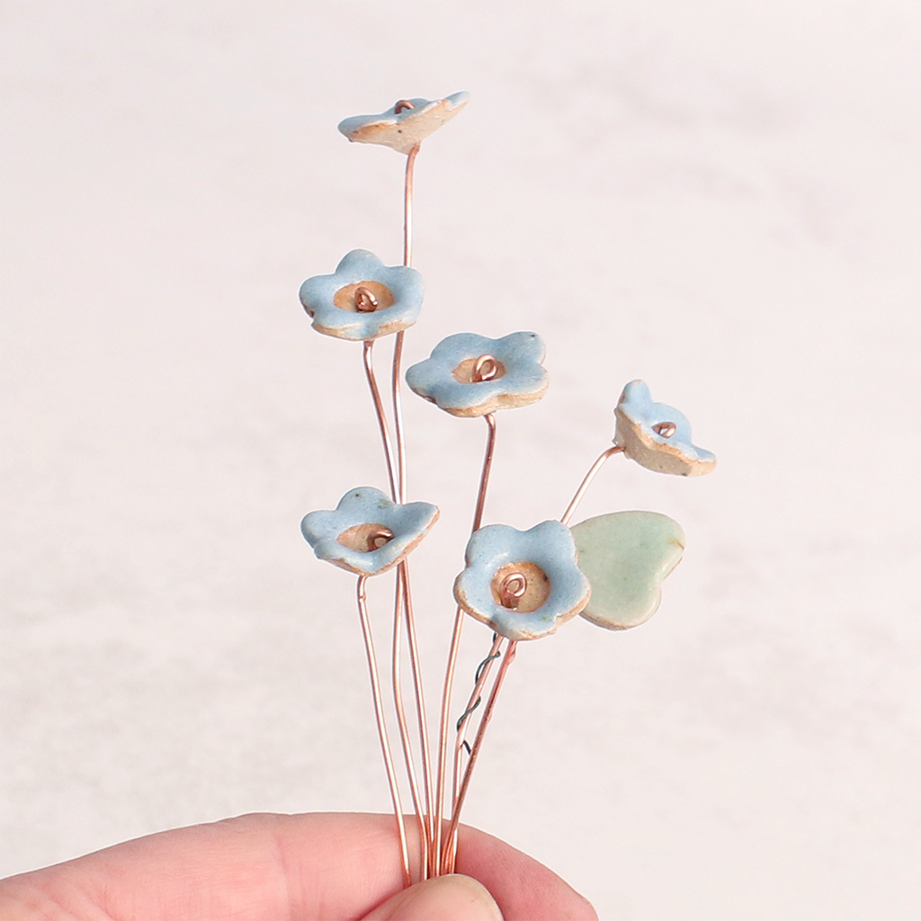 Close-up of hand holding pastel ceramic forget me not flower stems with copper wire stems – individually handcrafted floral home accessories from Habulous