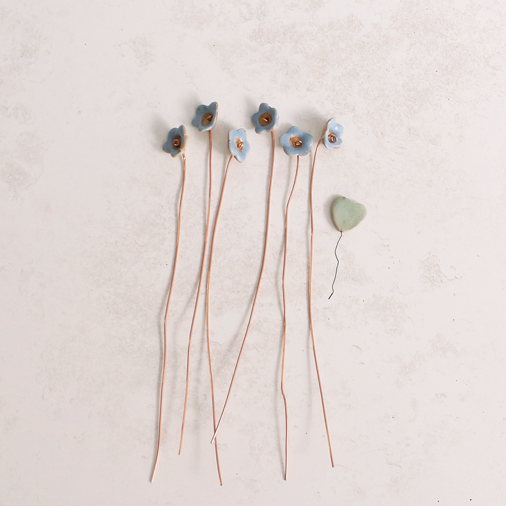 Close-up of pastel ceramic forget me not flower stems with copper wire stems on a table  – individually handcrafted floral home accessories from Habulous