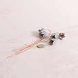 Handcrafted ceramic bluebell flower stems with soft glazes lay on a table. Each flower features a flexible copper wire stem for easy adjustment.