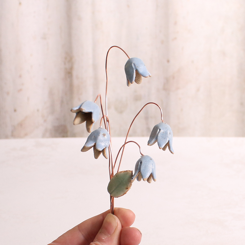 Handcrafted ceramic bluebell flower stems with soft glazes being held in someone's hands. Each flower features a flexible copper wire stem for easy adjustment.