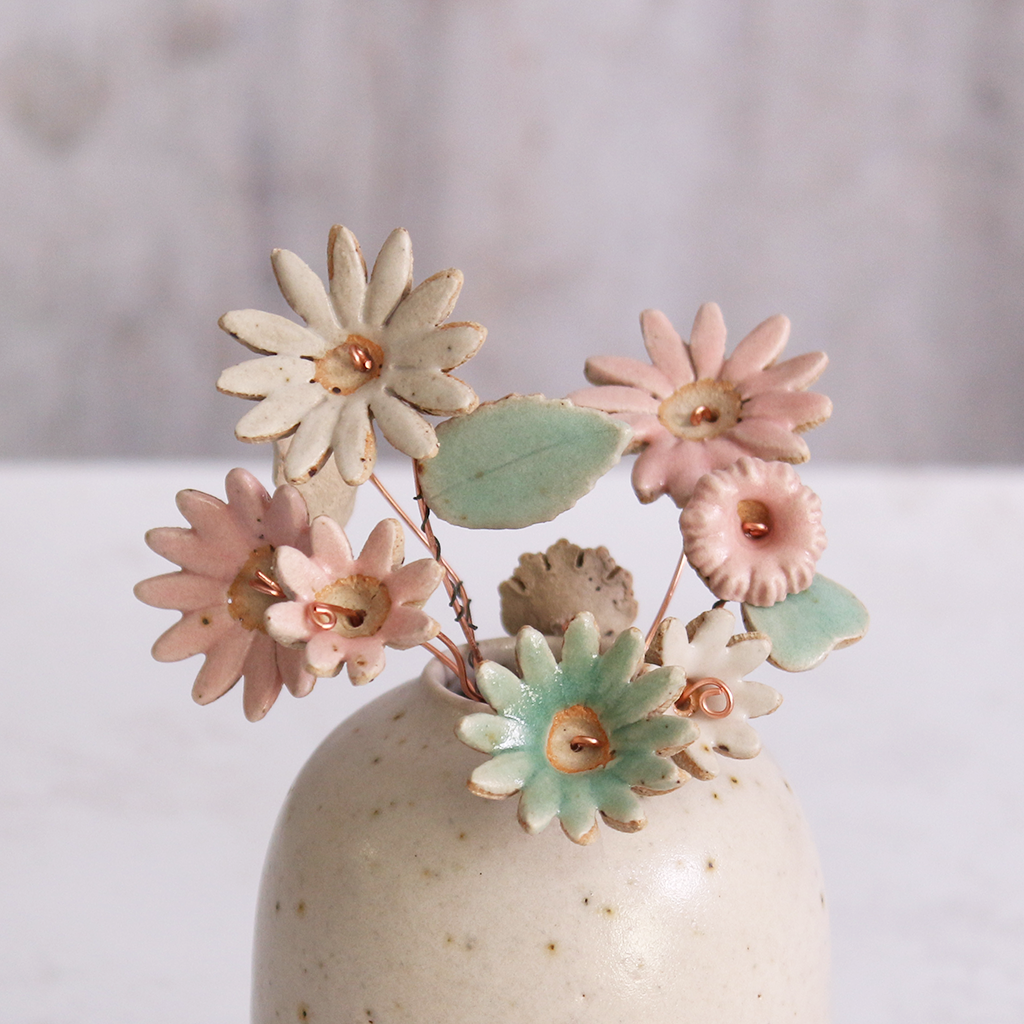 Handcrafted ceramic flower bouquet in a vase, featuring delicate pink and white wildflowers with green leaves, arranged with copper wire stems — perfect for rustic home decor.