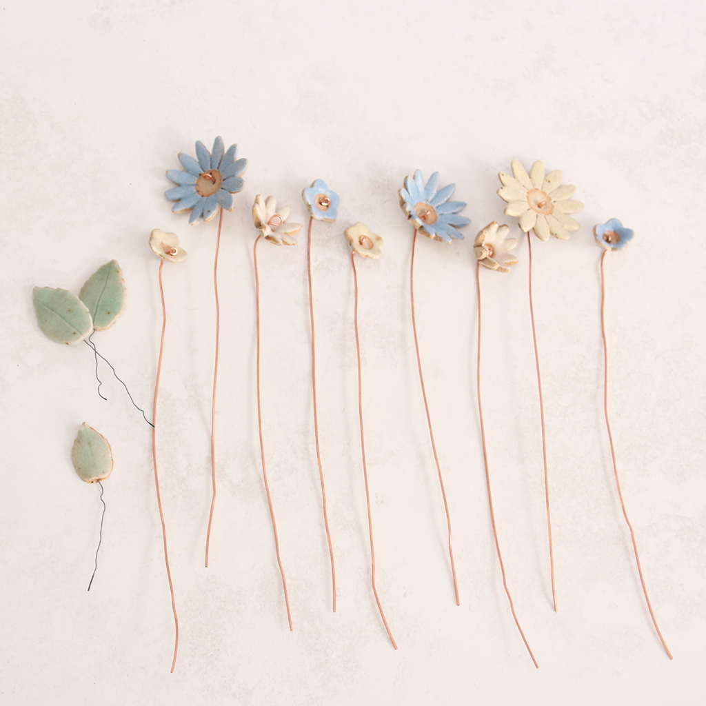 Handcrafted ceramic flower bouquet, featuring delicate blue and white wildflowers with green leaves, arranged with copper wire stems — perfect for rustic home decor.
