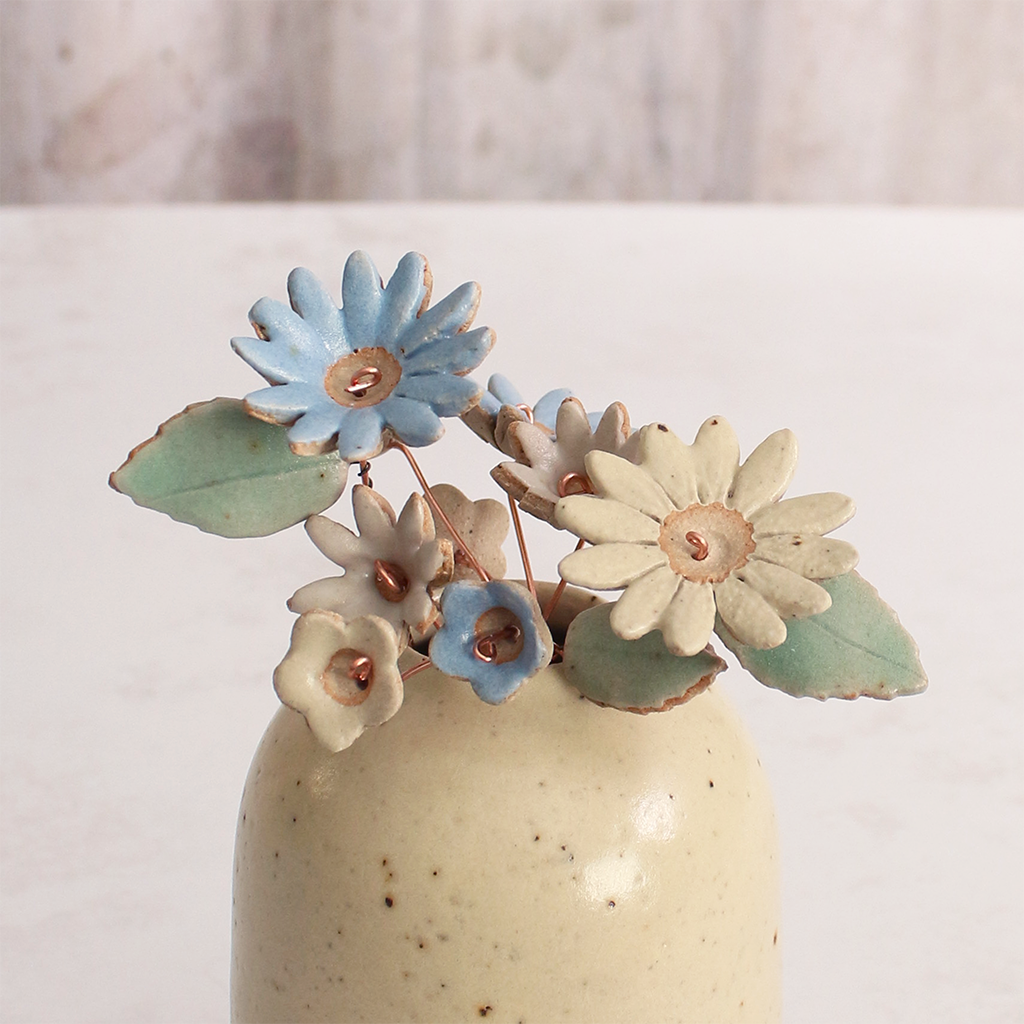 Handcrafted ceramic flower bouquet in a vase, featuring delicate blue and white wildflowers with green leaves, arranged with copper wire stems — perfect for rustic home decor.