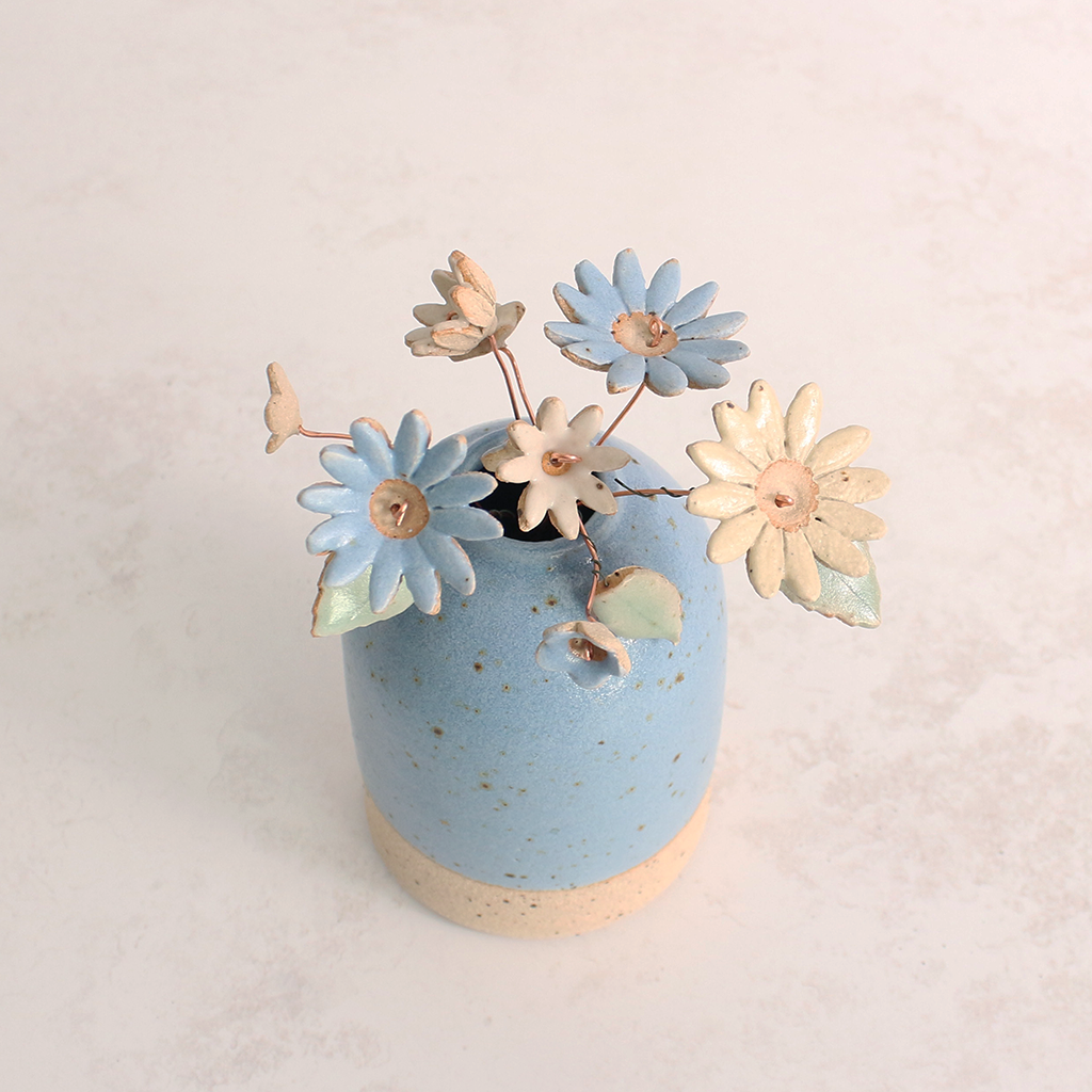Handcrafted ceramic flower bouquet in a vase, featuring delicate blue and white wildflowers with green leaves, arranged with copper wire stems — perfect for rustic home decor.