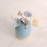 Handcrafted ceramic flower bouquet in a vase, featuring delicate blue and white wildflowers with green leaves, arranged with copper wire stems — perfect for rustic home decor.