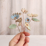 Handcrafted ceramic flower bouquet, featuring delicate blue and white wildflowers with green leaves, arranged with copper wire stems — perfect for rustic home decor.