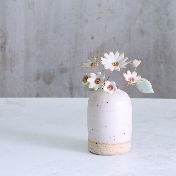 Small ceramic vase with speckled texture holding white flowers against a gray background