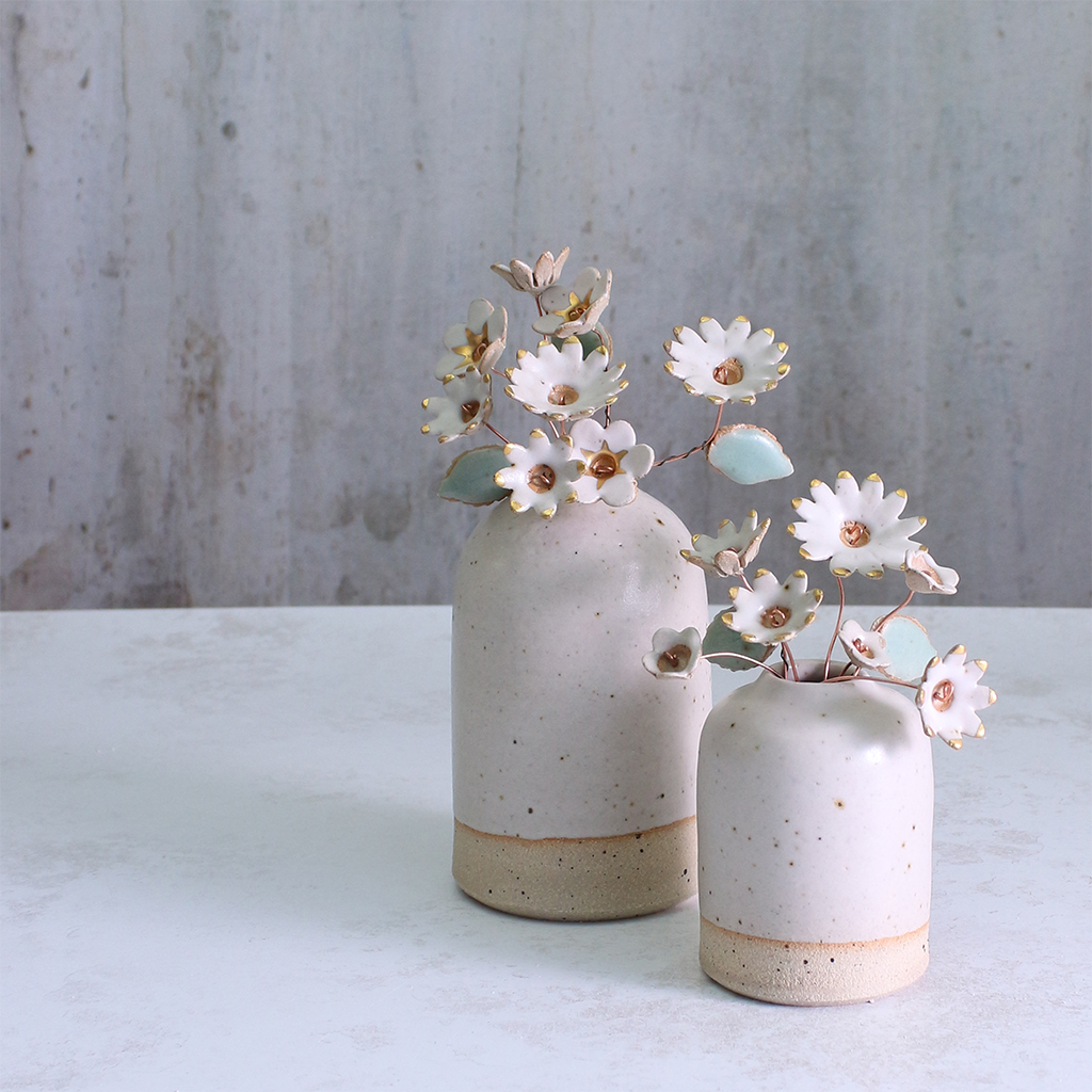 Two ceramic vases with speckled texture holding small white flowers on a light background