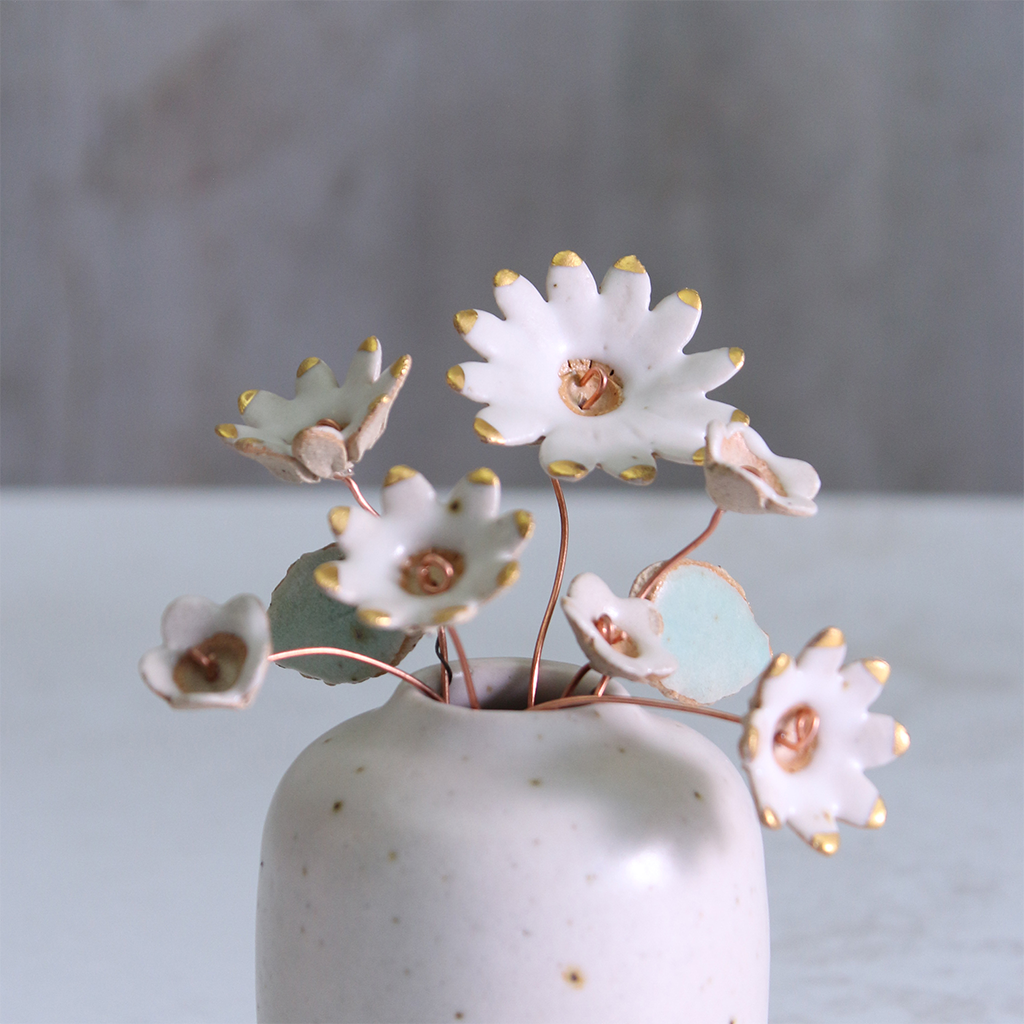 Handmade ceramic flower bouquet in white and gold with real gold-painted petals and copper wire stems, displayed in a small off-white ceramic vase.