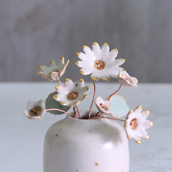 Handmade ceramic flower bouquet in white and gold with real gold-painted petals and copper wire stems, displayed in a small off-white ceramic vase.