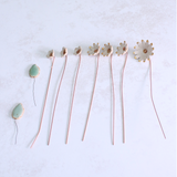 Handmade ceramic flower bouquet in white and gold with real gold-painted petals and copper wire stems, spread in size order on a table.
