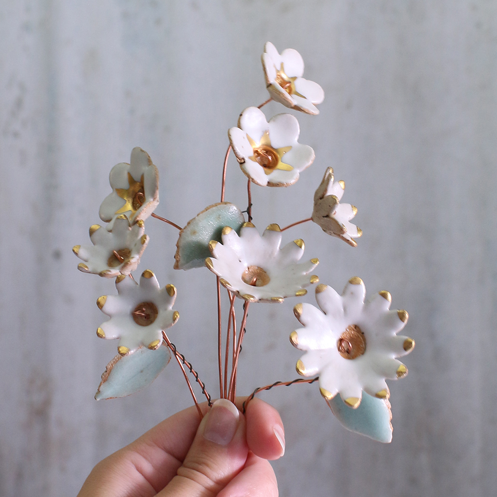 Handmade ceramic flower bouquet in white with gold-painted petals and copper wire stems being held in someone's hands.
